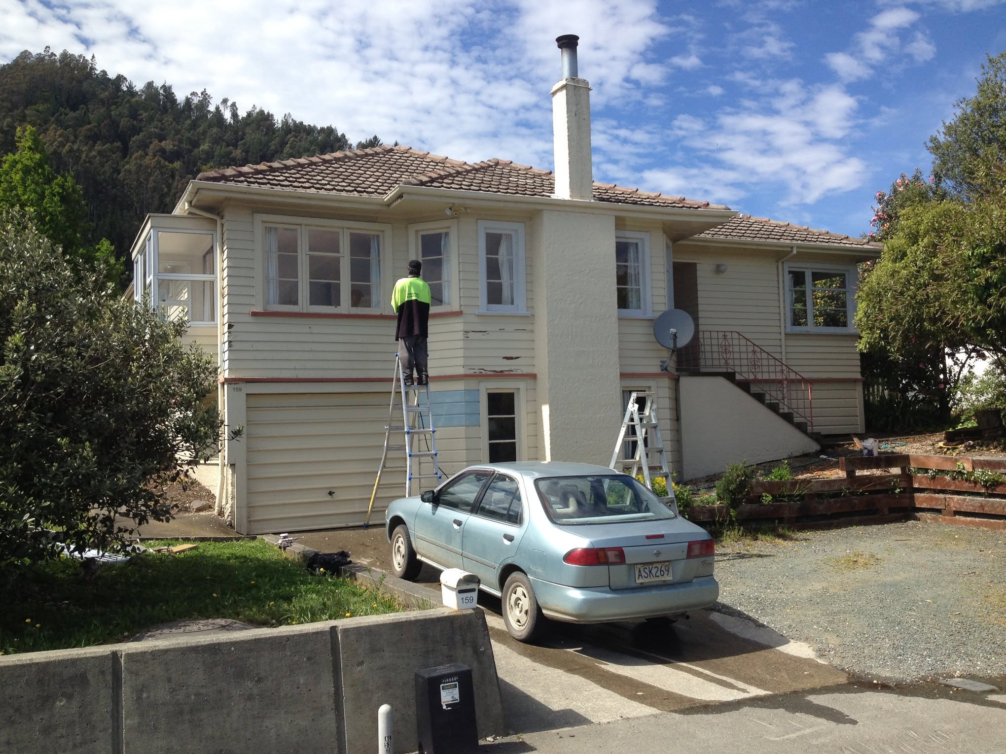 Two-storey weatherboard house mid-job, painter on a ladder