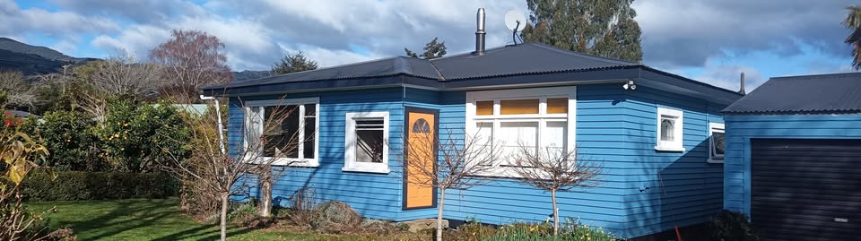 Freshly painted blue weatherboard house with white trim in Golden Bay