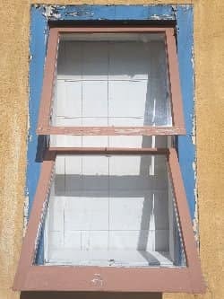 Two-pane wooden awning window with flaking blue and clay paint